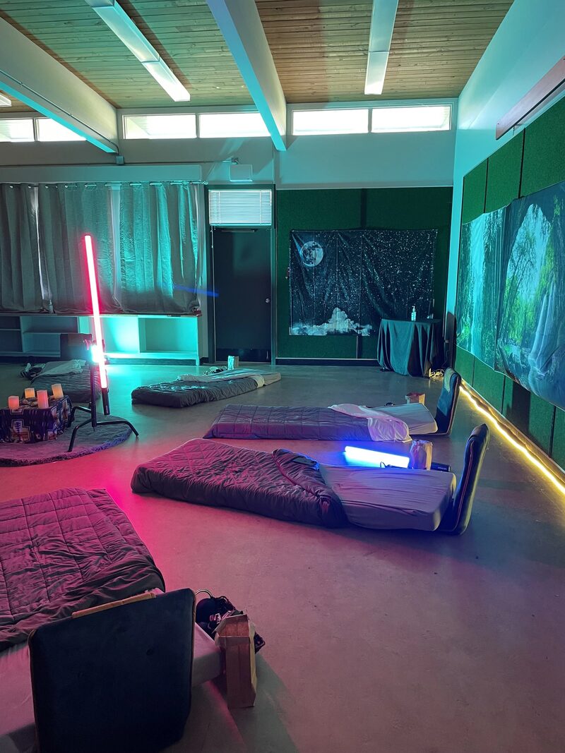 A room decorated with colorful neon lights and tents set up on the floor, resembling a sleepover or retreat space with room dividers and wall art.